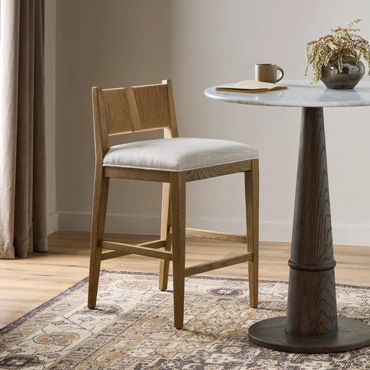 Selene Bar Stool by Four Hands in dover crescent, aged oak, natural paper cord. Made from 71% viscose (rayon), 17% polyester, 12% flax/linen, solid oak, rush in a transitional style.