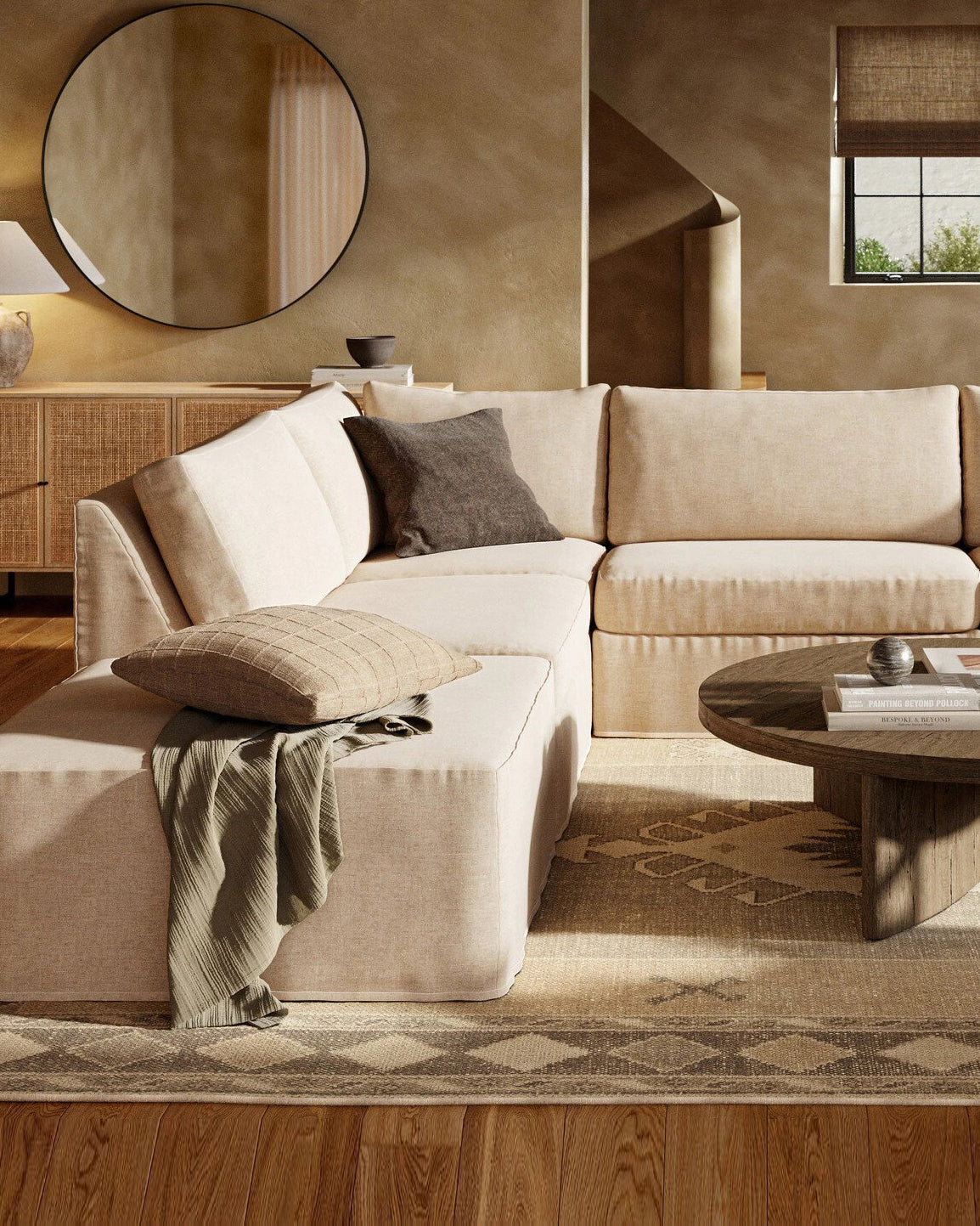Cozy living room featuring a large beige sectional sofa, round wooden coffee table, neutral decor accents, and a woven sideboard, creating a warm, inviting atmosphere.