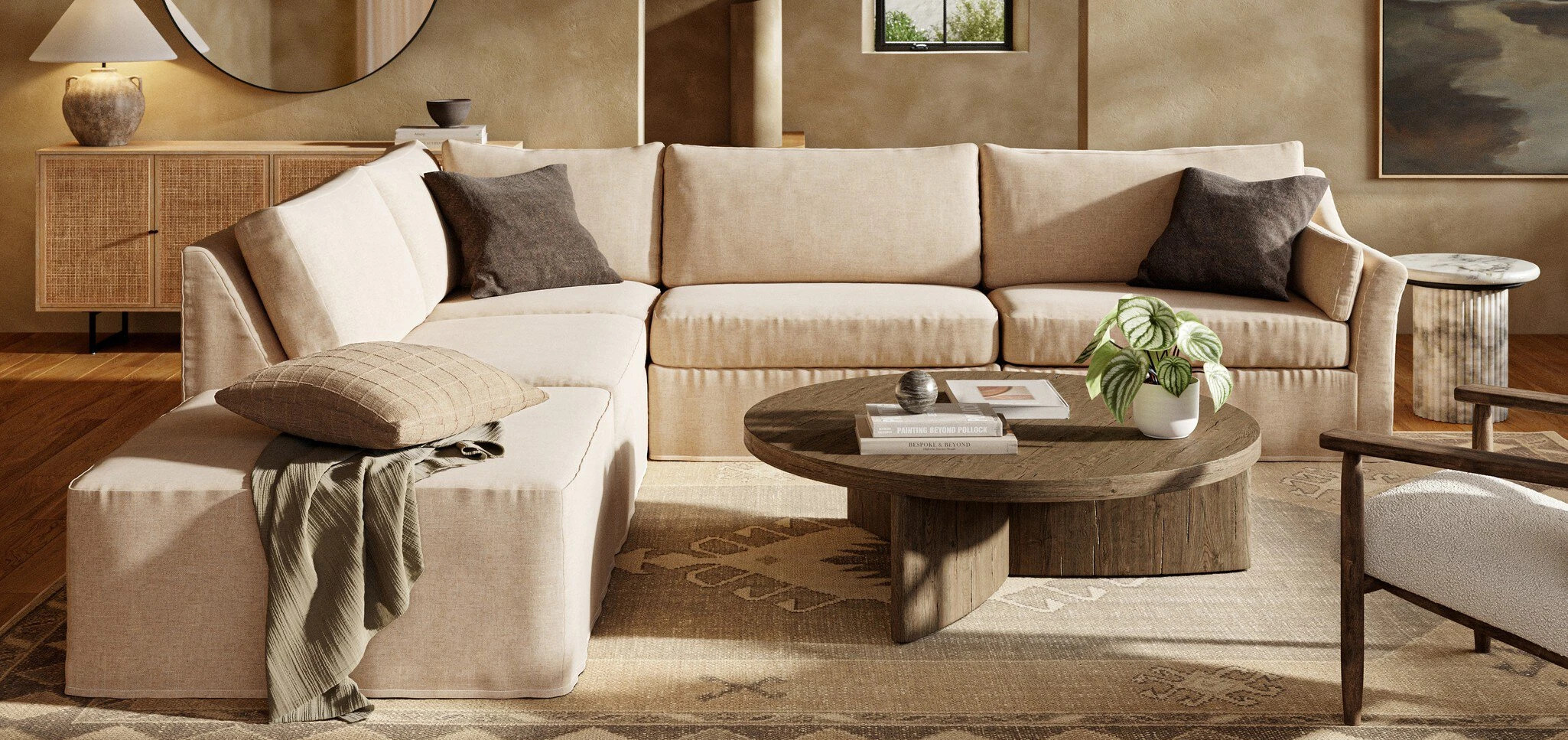 Cozy living room featuring a large beige sectional sofa, round wooden coffee table, neutral decor accents, and a woven sideboard, creating a warm, inviting atmosphere.