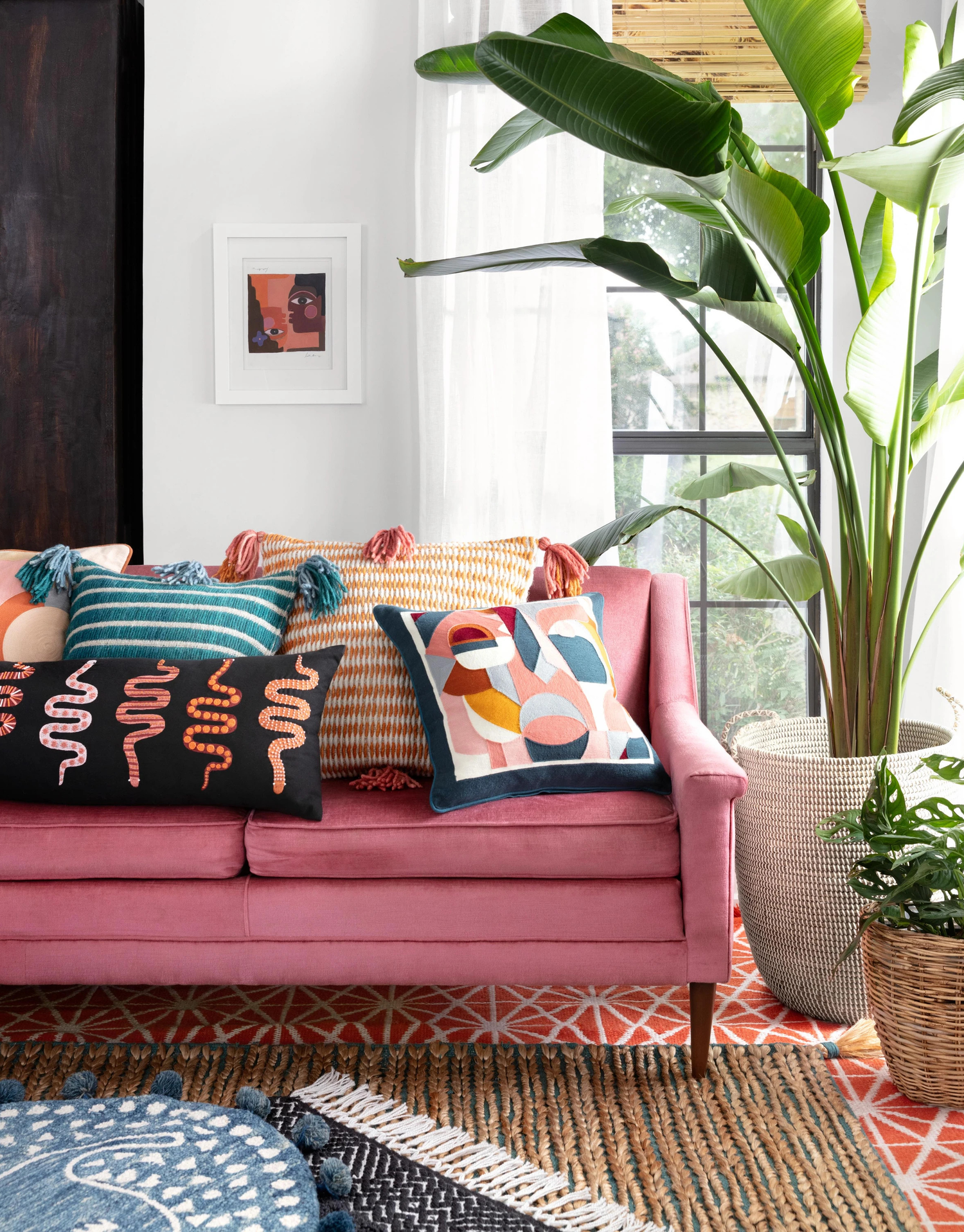 Eclectic living room with a bold pink sofa, colorful patterned throw pillows, layered rugs, and vibrant greenery, creating a playful and artistic atmosphere.