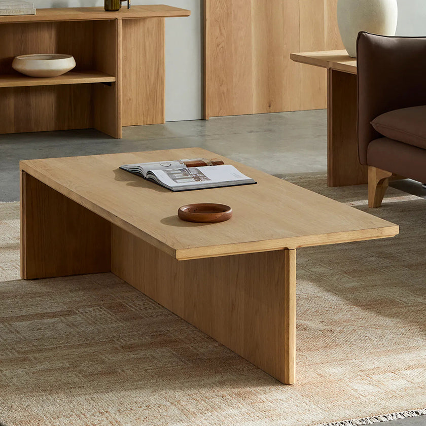 Minimalist wooden coffee table with clean lines, featuring a large surface and geometric design, complemented by a decorative bowl and a magazine. Ideal for modern living rooms and stylish interiors.