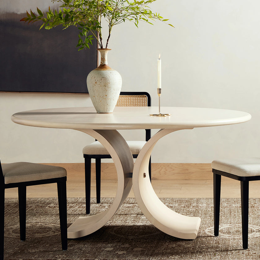 Elegant round dining table with a sculptural, curved pedestal base, complemented by minimalist chairs, perfect for modern dining rooms.