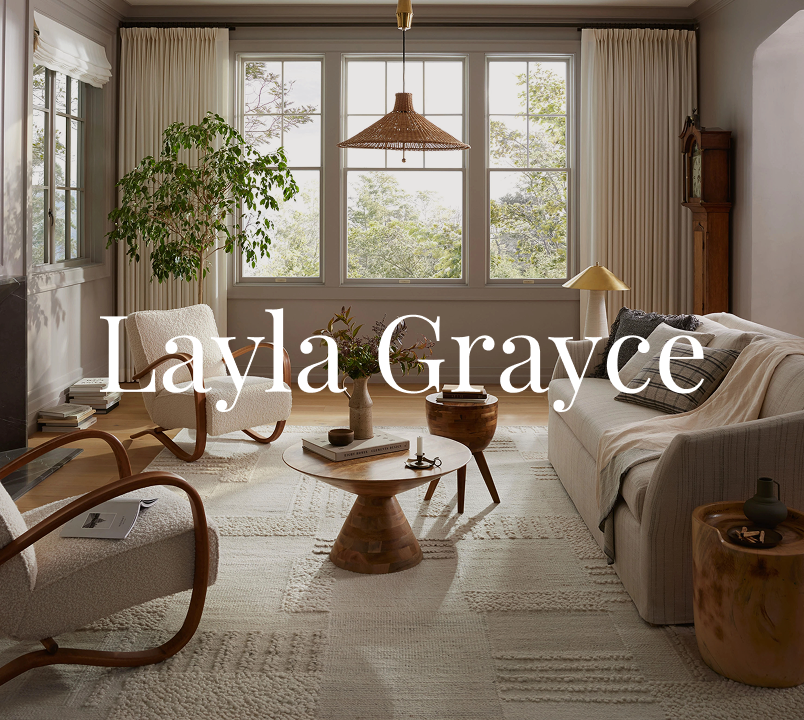 Bright living room styled with Layla Grayce furniture, featuring a neutral sofa, boucle accent chairs with wood arms, round wood coffee tables, and large windows framed by cream curtains.