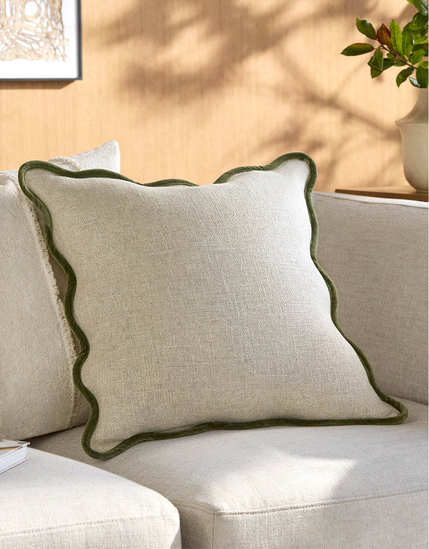 Neutral throw pillow with scalloped green trim on beige sofa