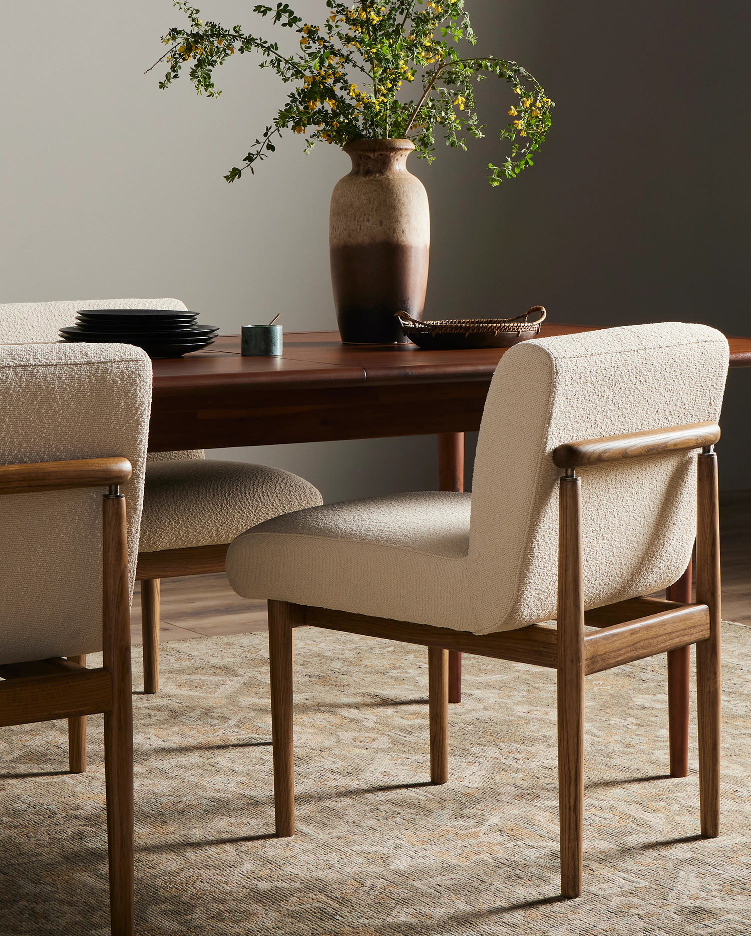 Modern dining room featuring upholstered wooden dining chairs, a dark wood dining table, and a decorative vase with greenery, creating a cozy, elegant atmosphere.