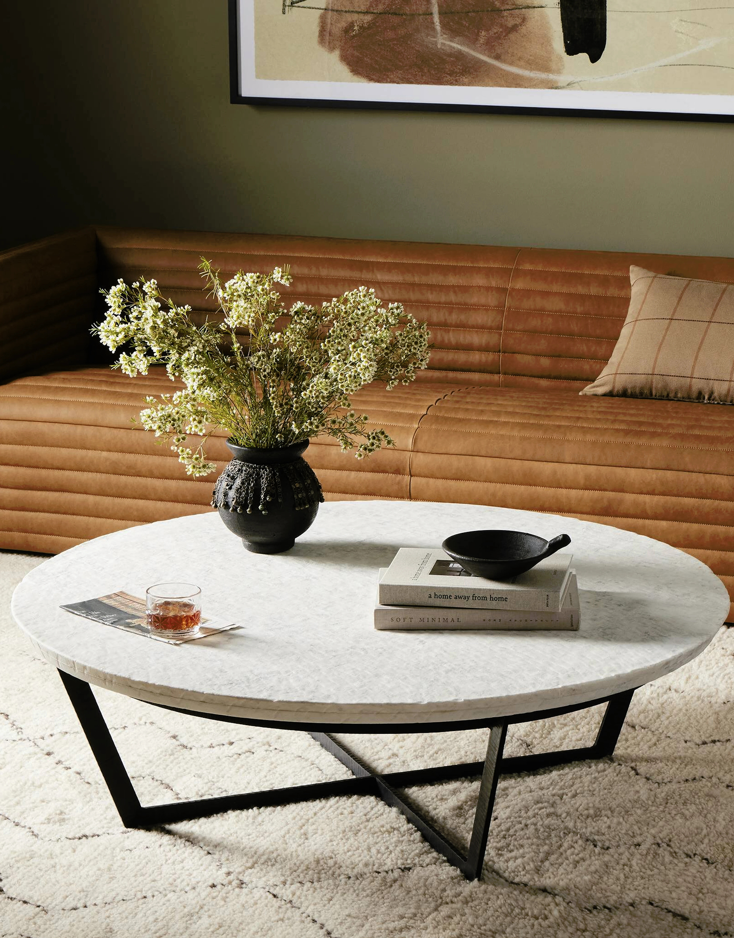 Modern living room featuring a round marble coffee table with a black metal base, styled with decorative books and a vase, paired with a leather sofa and neutral decor.