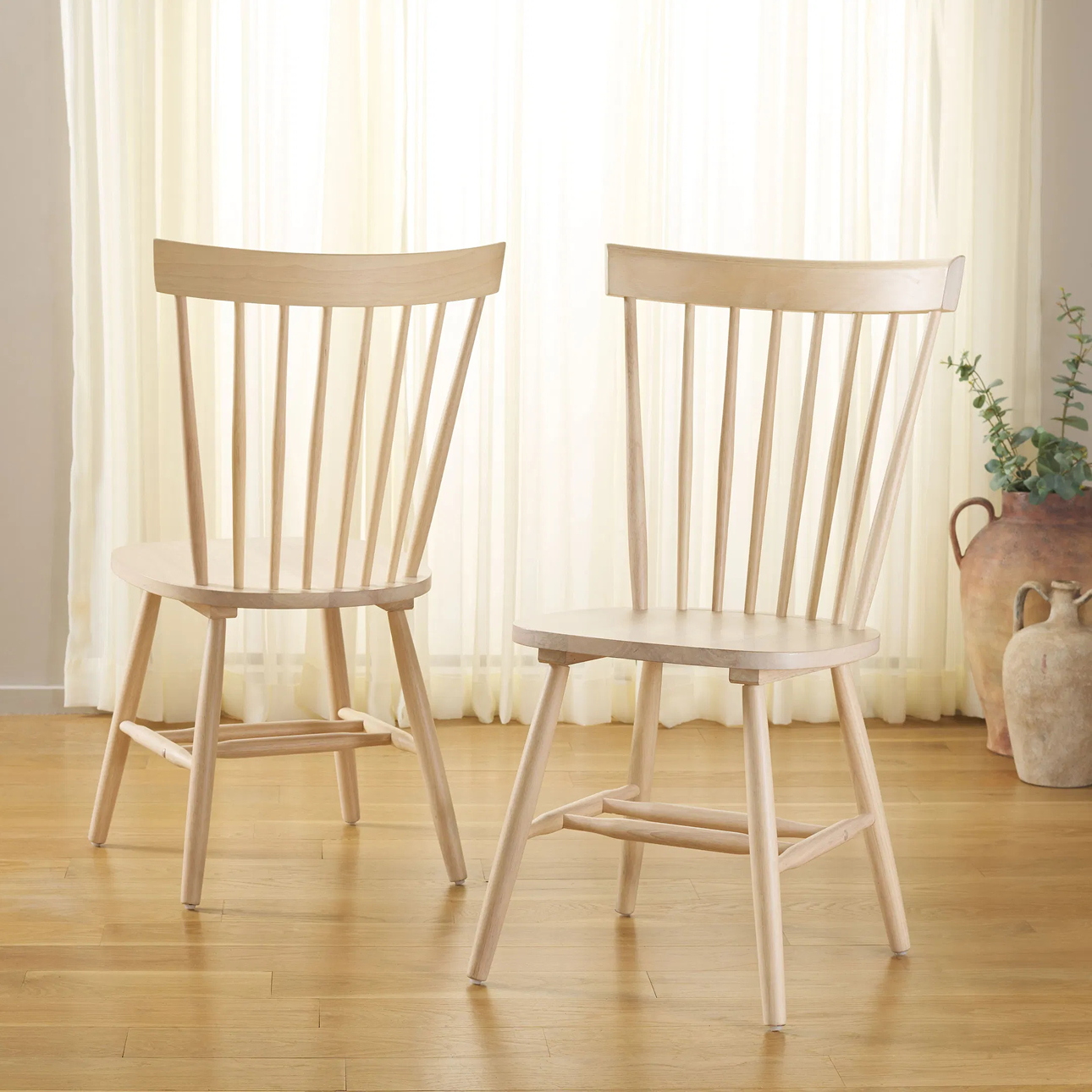 Set of two natural wood dining chairs with tall spindle backs and tapered legs, styled in a bright, minimal dining space—shop now on sale.