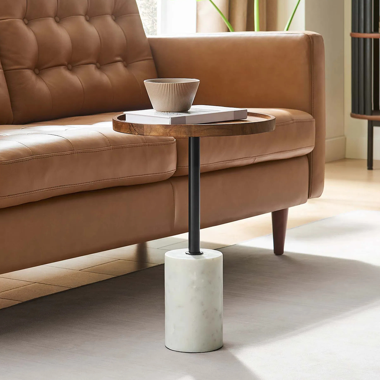 Modern side table with a round wood top, black metal stem, and white marble base, styled next to a tan leather sofa—shop now on sale.